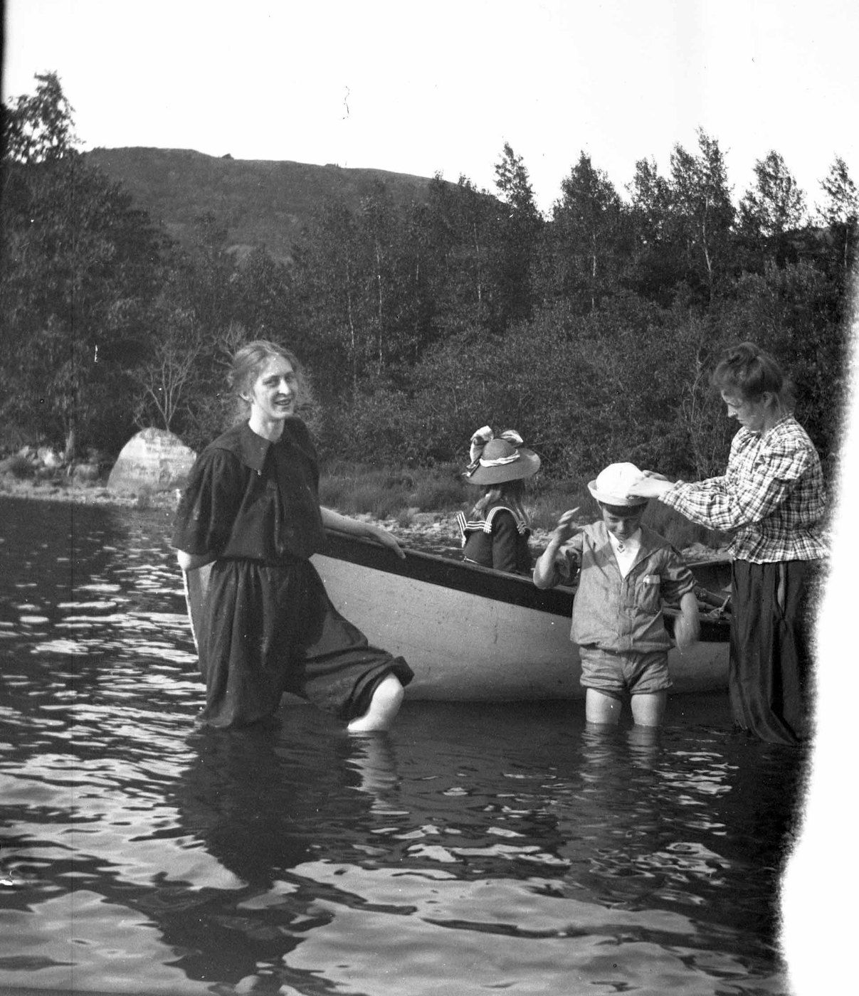 A vintage black and white photograph showing a group of people in and around a small boat in a body of water.