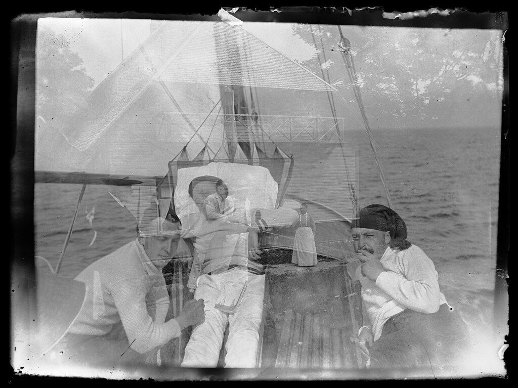 A vintage black and white photograph of three sailors tending to an injured comrade on the deck of a sailing ship.