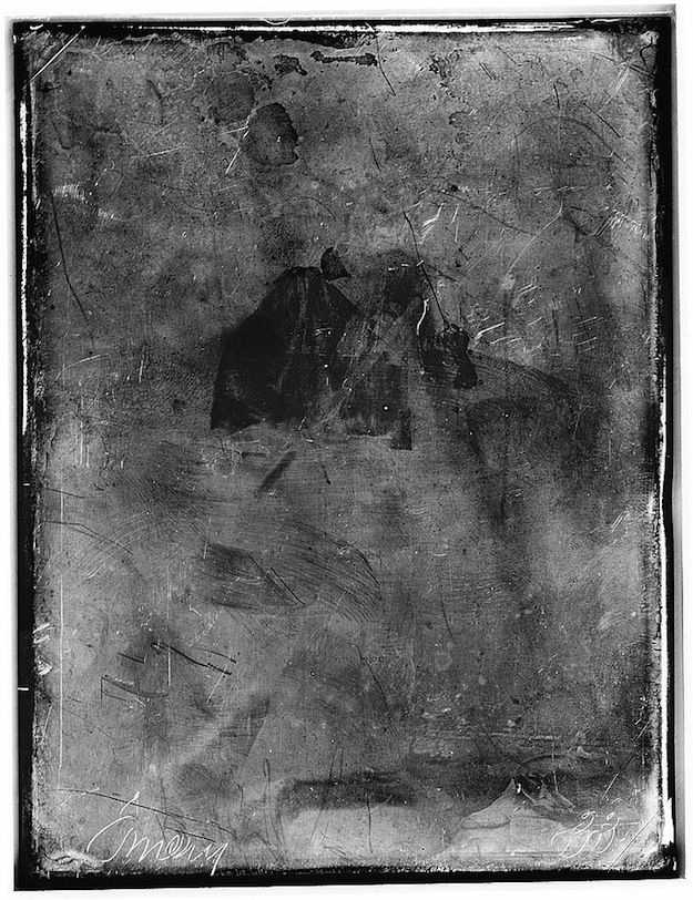 A distressed, vintage-style portrait of a person with a partially visible face, heavily scratched and marked with areas of dark discoloration.