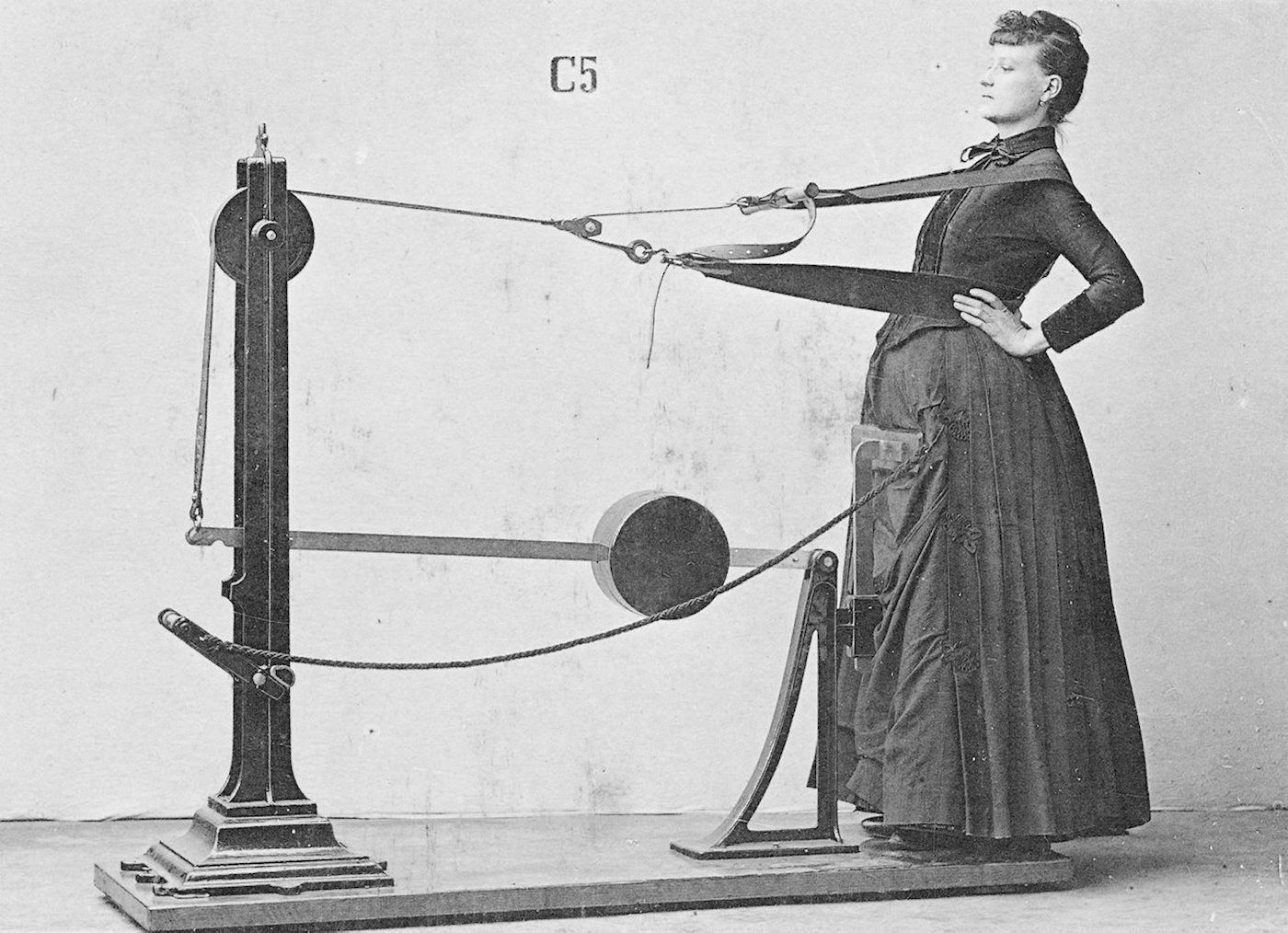 Vintage black and white photograph of a woman interacting with a complex mechanical apparatus.