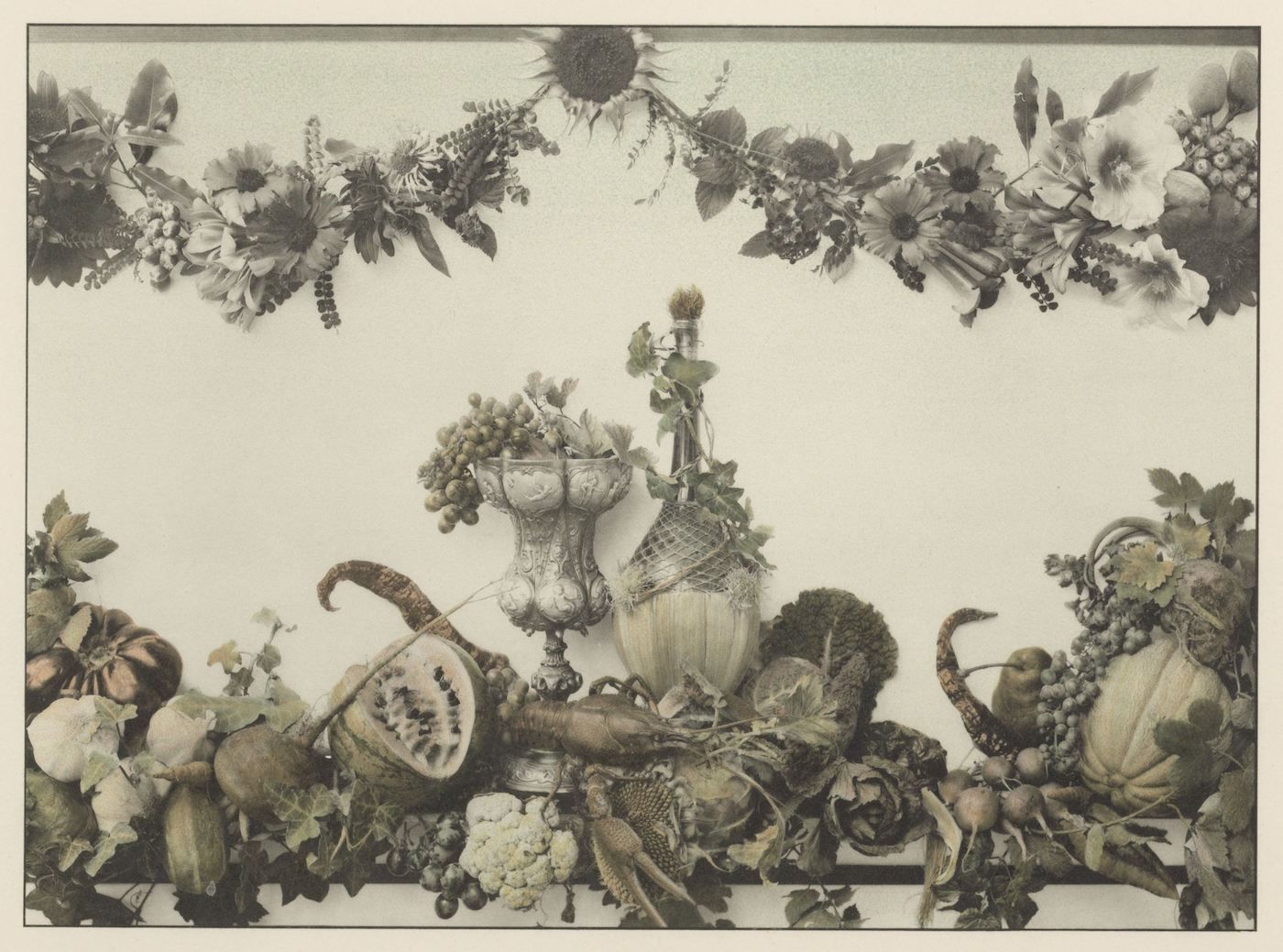 Sepia-toned still life arrangement with a garland of flowers and leaves above a display of fruits, vegetables, and floral arrangements.