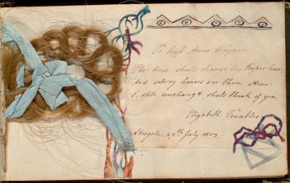 A Victorian-era hair work and sentimental card with a lock of reddish-brown hair tied with a faded light blue ribbon, handwritten script, and a decorative border.