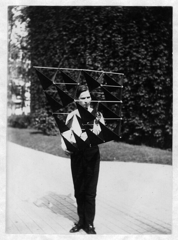 A vintage black and white photograph of a person wearing a large, triangular wing-like structure on their back.