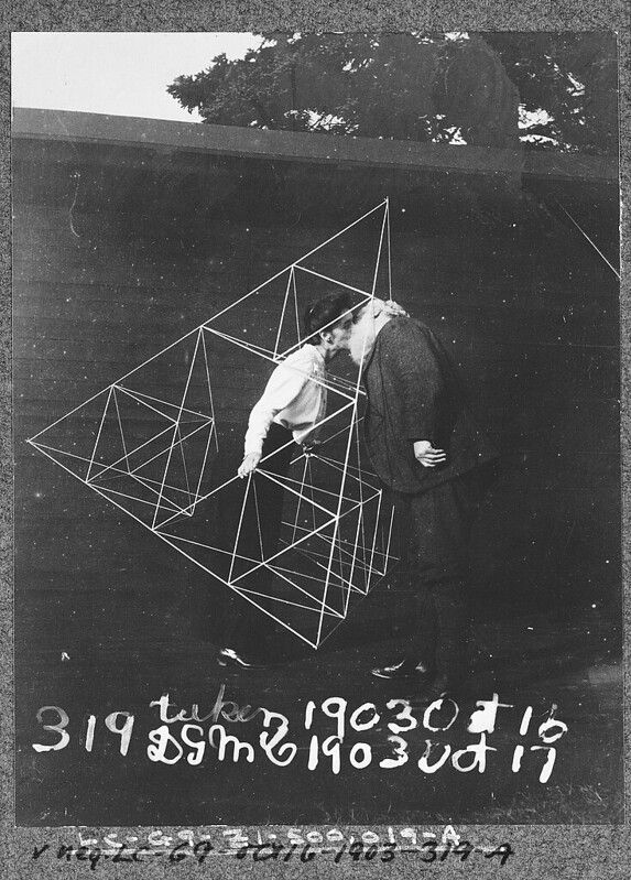 A black and white photograph of a couple kissing within a geometric structure.