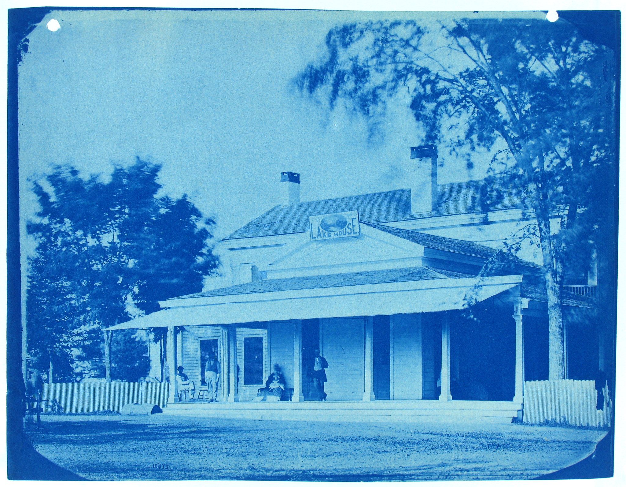 Cyanotype photograph of a large, two-story house with a wide porch and a sign reading 'Lake House'.