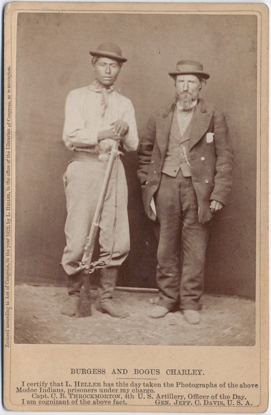 A vintage photograph of two Native American men, Burgess and Bogus Charley, identified as Modoc Indians and prisoners under the charge of Capt. C.B. Throckmorton, 4th U.S. Artillery.