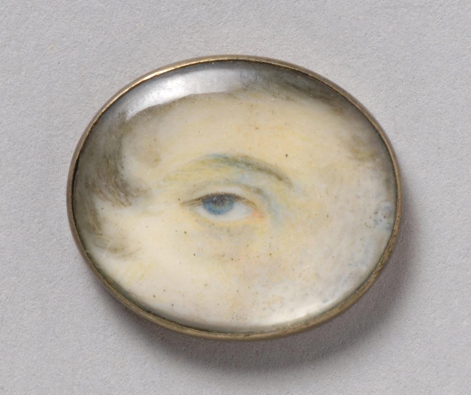 Close-up of a painted eye within a circular brass frame.