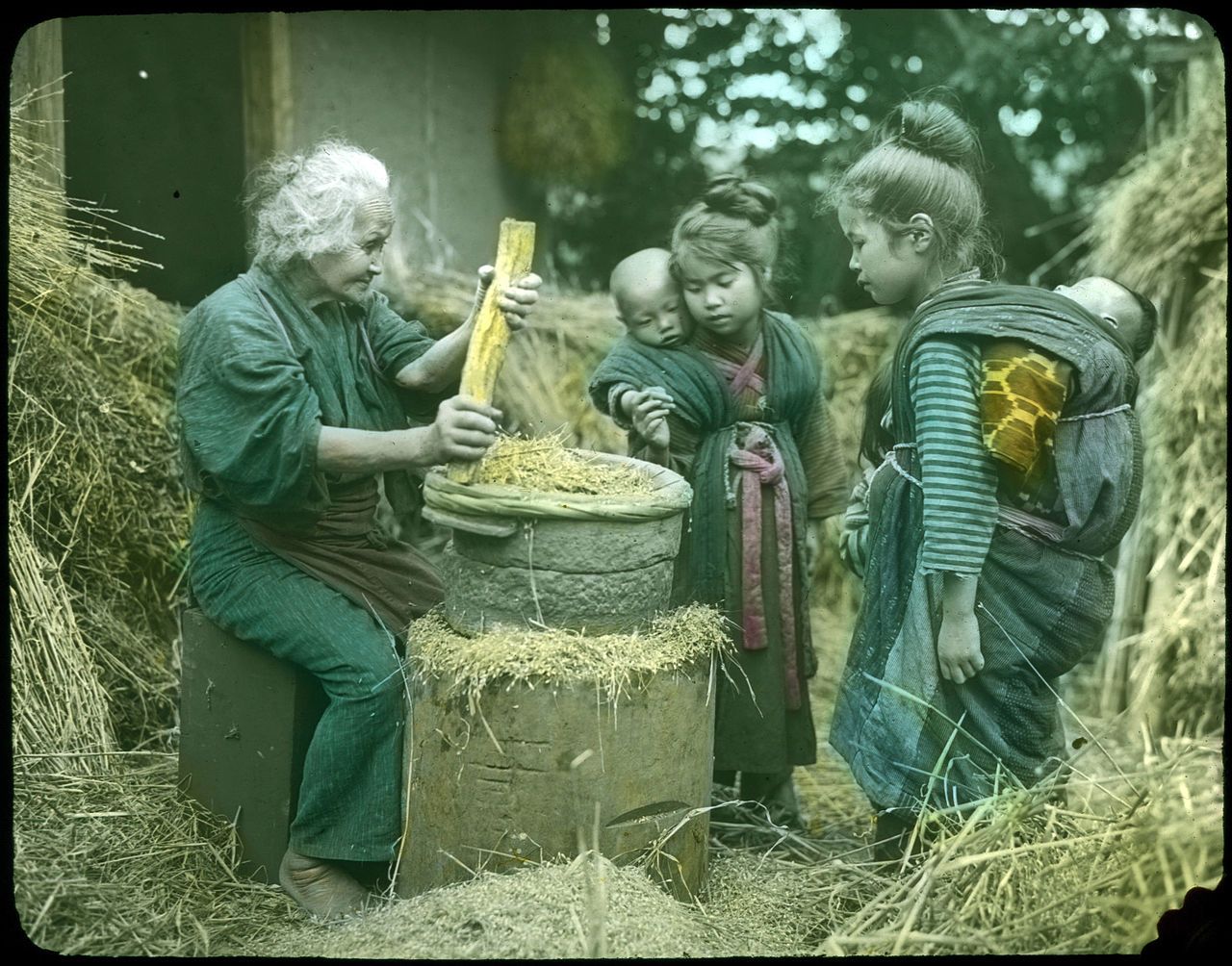 Vintage color photograph of an elderly man threshing grain with three children watching in a rural setting.