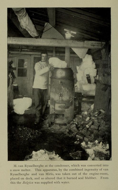 A sepia-toned photograph of a man standing next to a large, cylindrical metal condenser, with a building and debris in the background.
