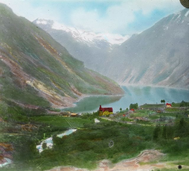 A scenic view of a valley with a lake and mountains.