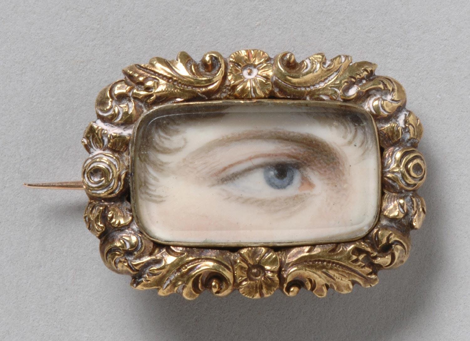 Close-up of a vintage brooch with a painted eye in an ornate golden frame.