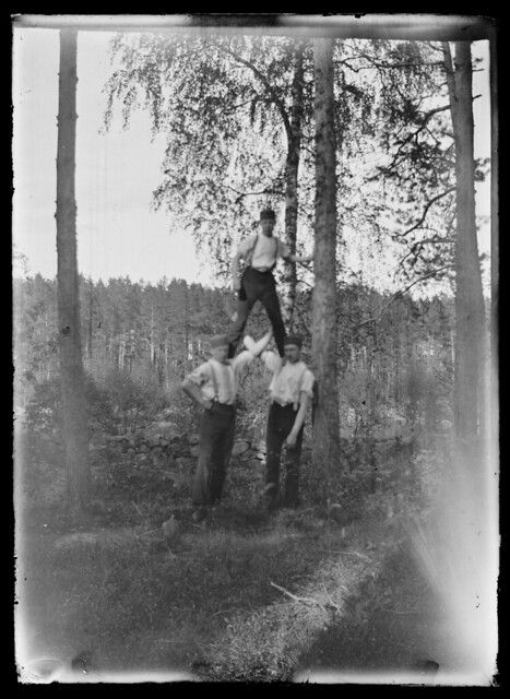 A vintage black and white photograph of four men forming a human pyramid in a forest setting.