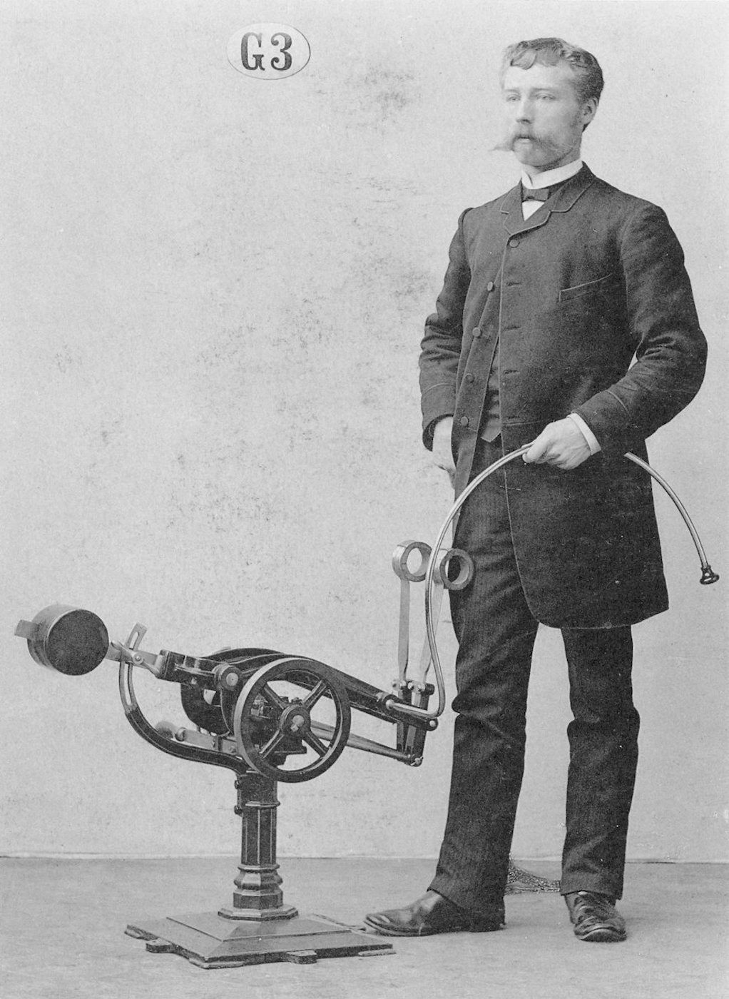 Vintage black and white photograph of a man in a suit standing next to a complex medical machine.