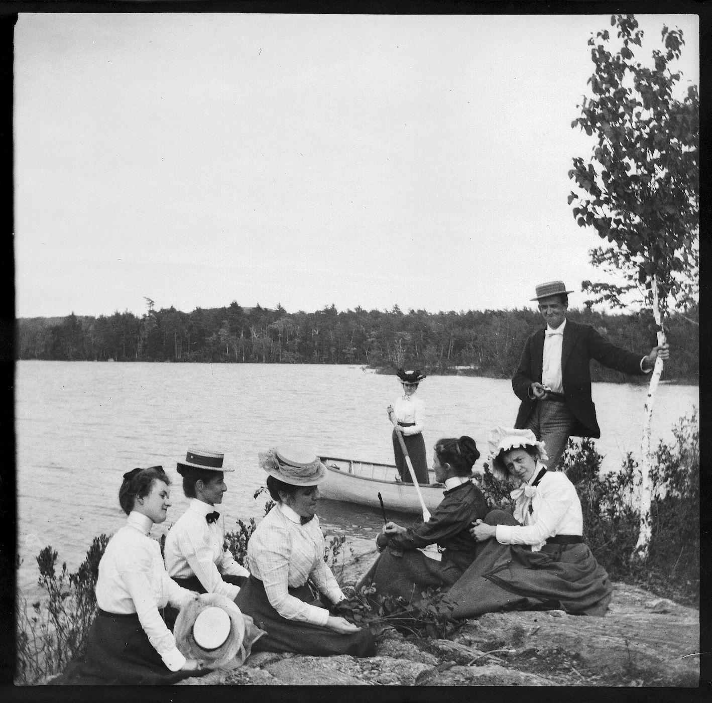 A black and white photograph of a group of people by a lake.
