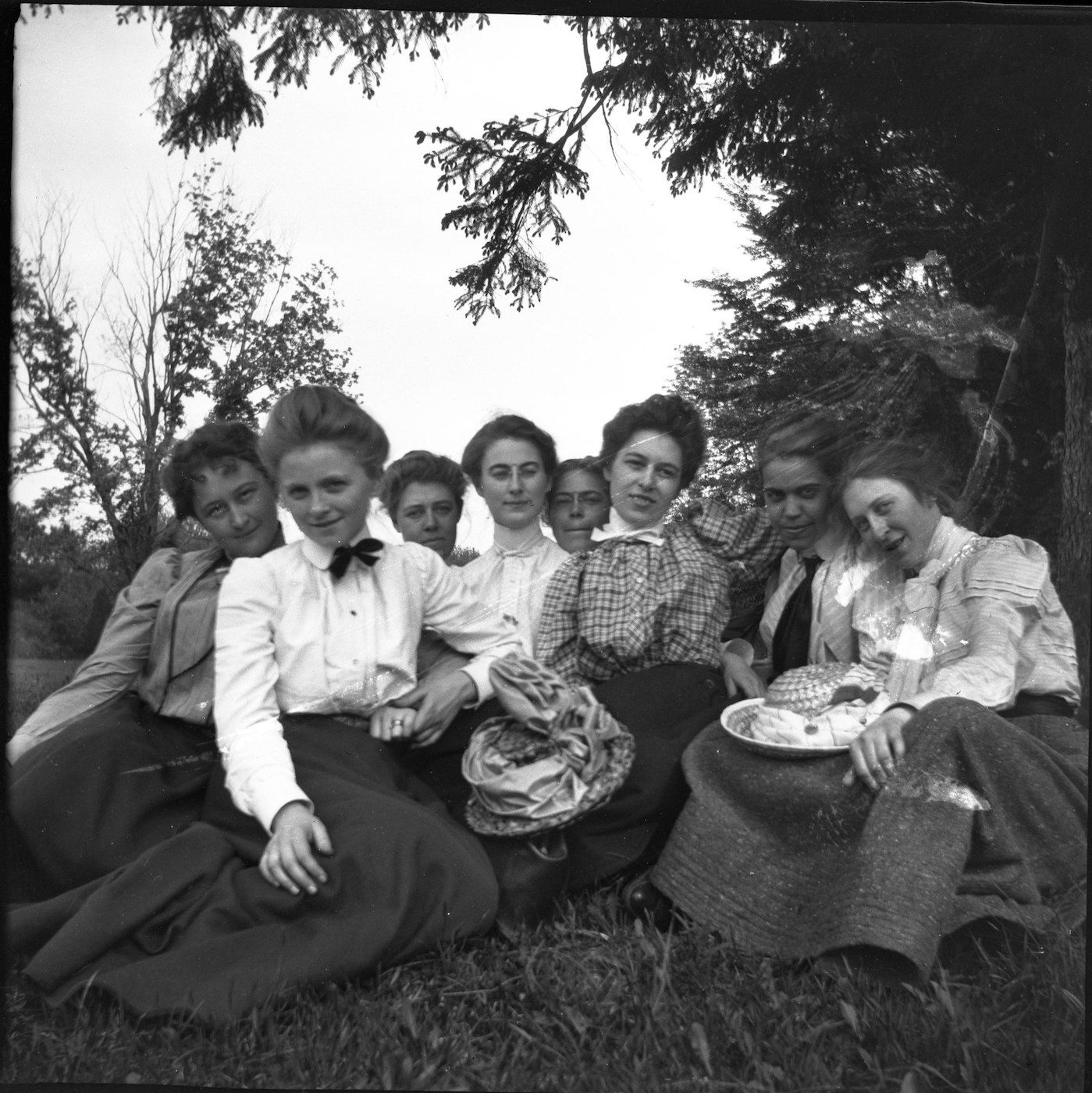 A black and white photograph of a group of eight women seated in a grassy field during a picnic.