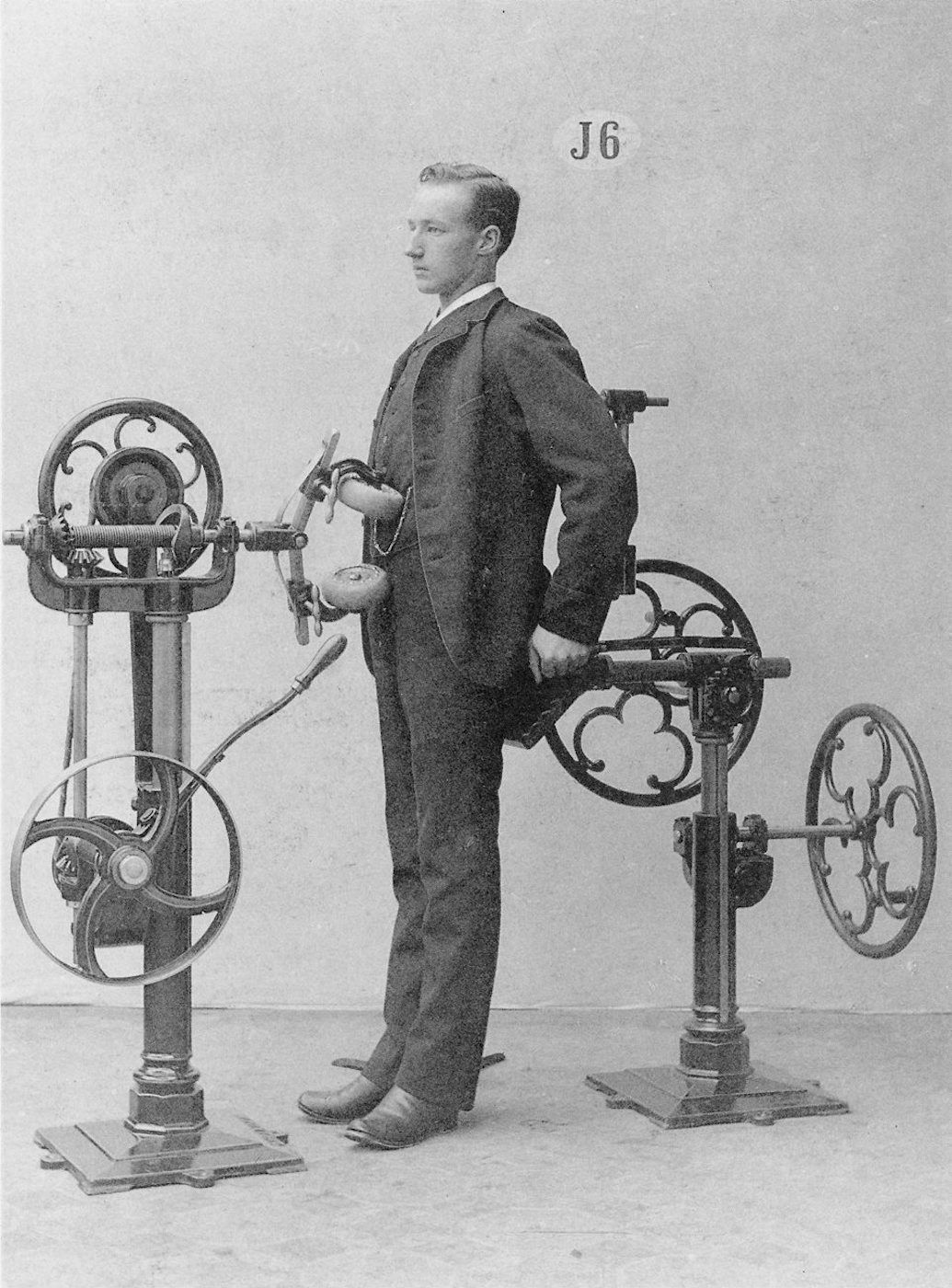 A vintage black and white photograph of a man standing next to a complex mechanical apparatus.