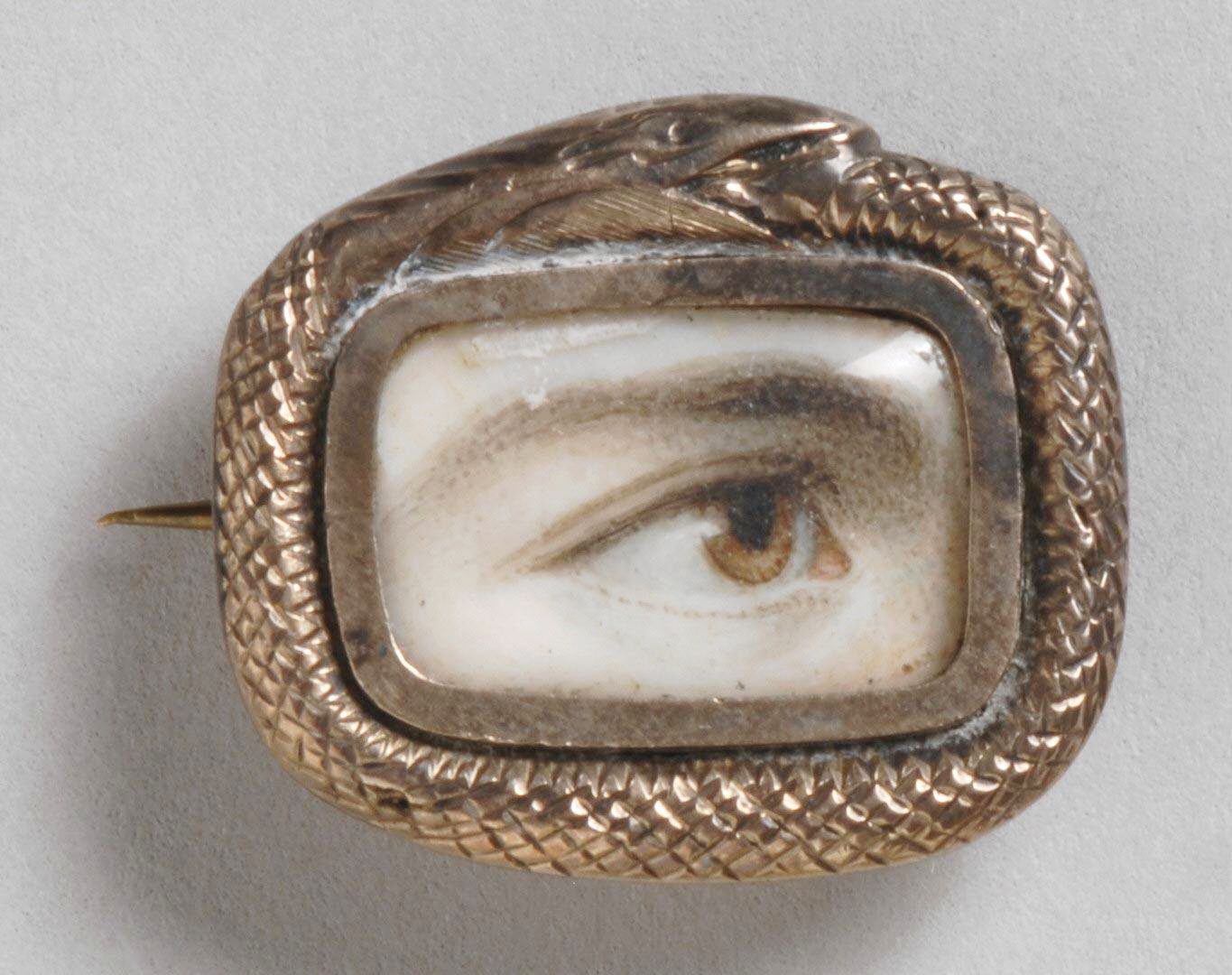 Close-up of a vintage brooch with a painted eye inside a textured gold frame.