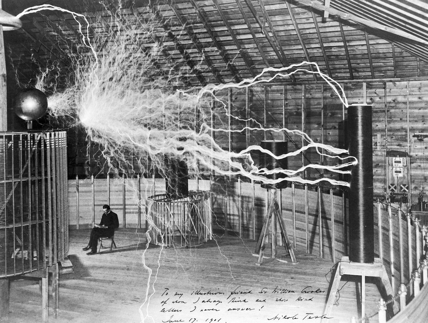 Historic black and white photograph of Nikola Tesla conducting an electrical experiment in his laboratory.