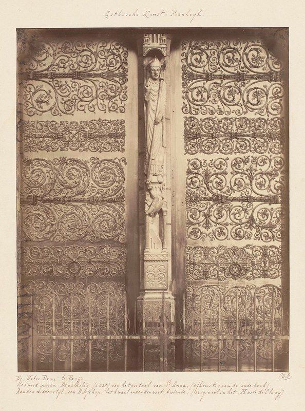 A vintage black and white photograph of a highly ornate gothic door with a statue in the center.