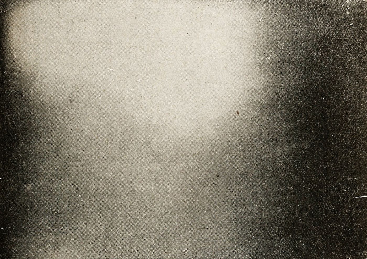 A grainy, vintage-style image with a light center and dark, speckled edges.