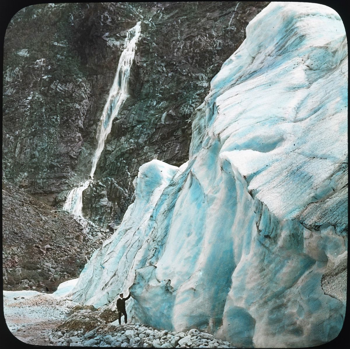 Vintage photograph of a glacier and waterfall with a person standing at the base.