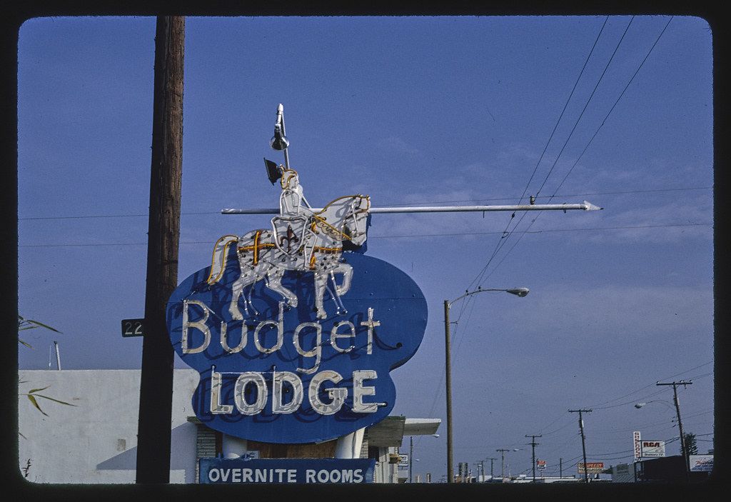 Vintage roadside sign for a "Budget Lodge" motel with a cowboy on horseback sculpture.