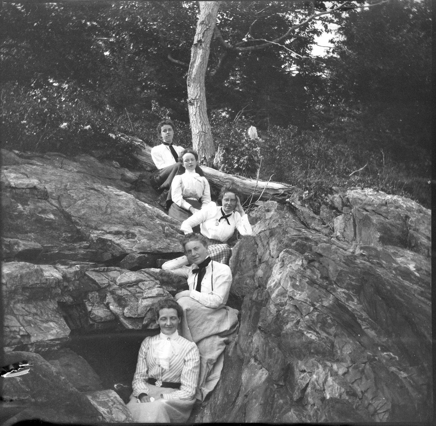 A vintage black and white photograph featuring a group of five people posed on a large, rocky outcrop in a wooded area.