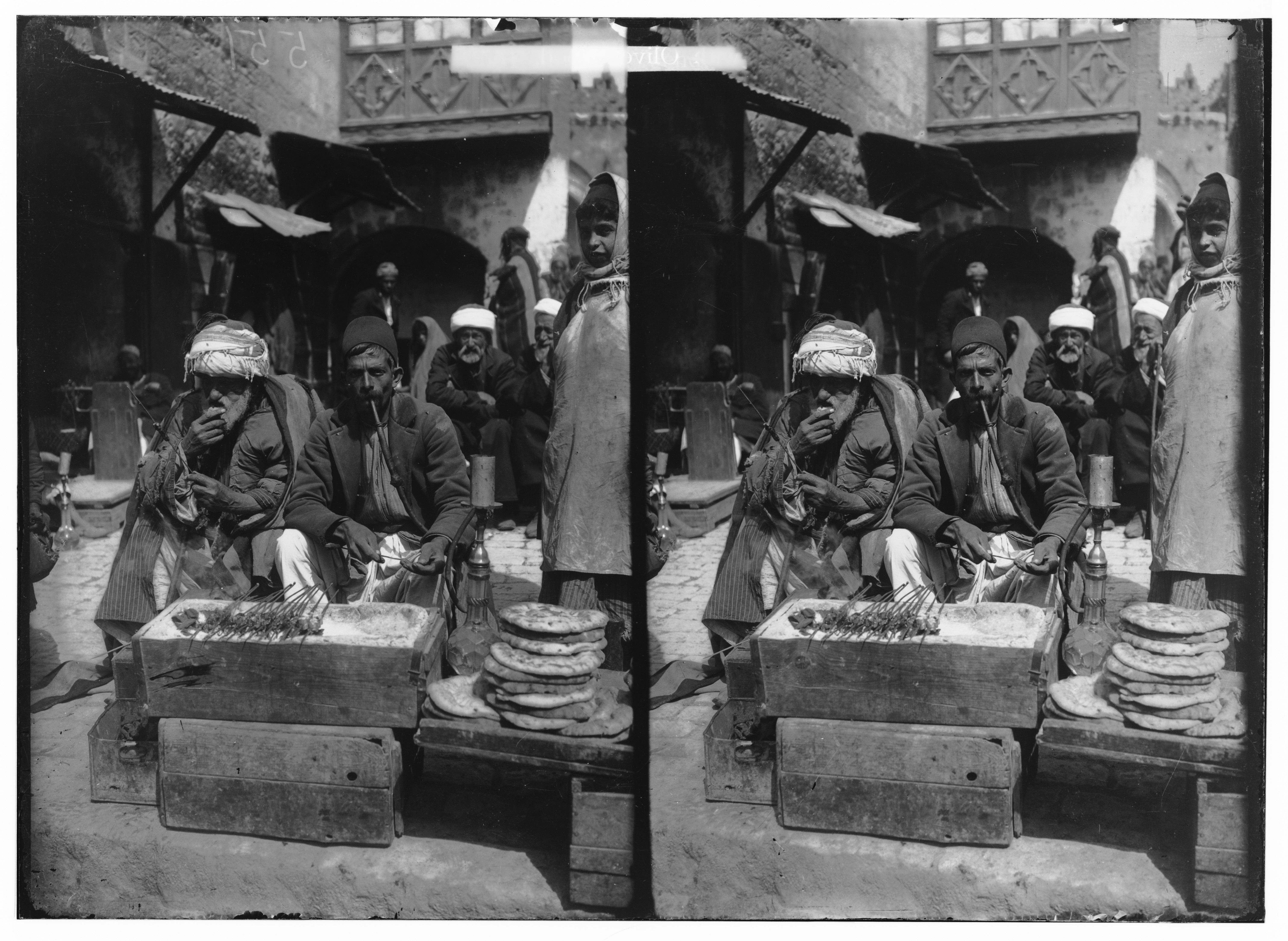 A black and white stereoscope card depicting a bustling market scene with men selling bread at low wooden tables.