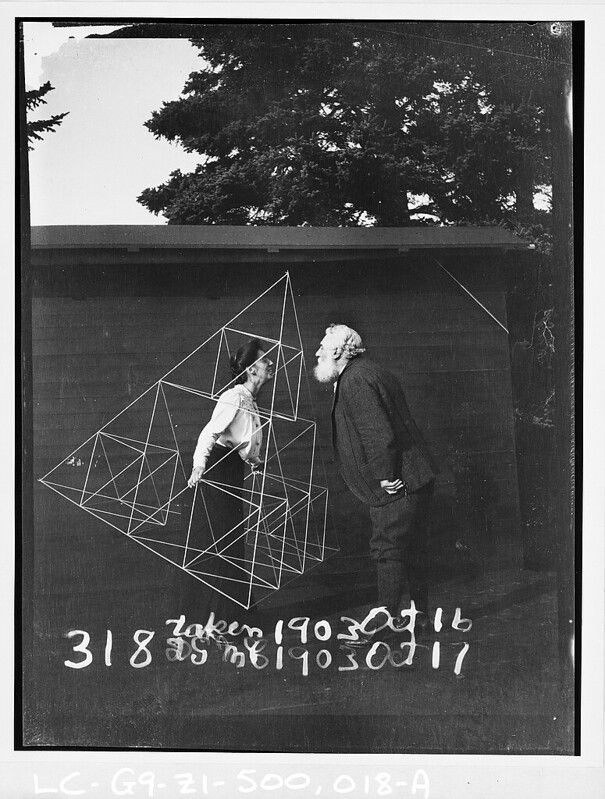 A black and white photograph of a woman and an older man standing in a park, with a complex geometric structure superimposed over the scene.