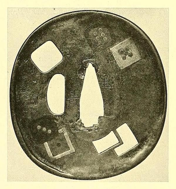A circular, dark metal tsuba with several geometric cut-outs, including a long central opening for a sword blade.