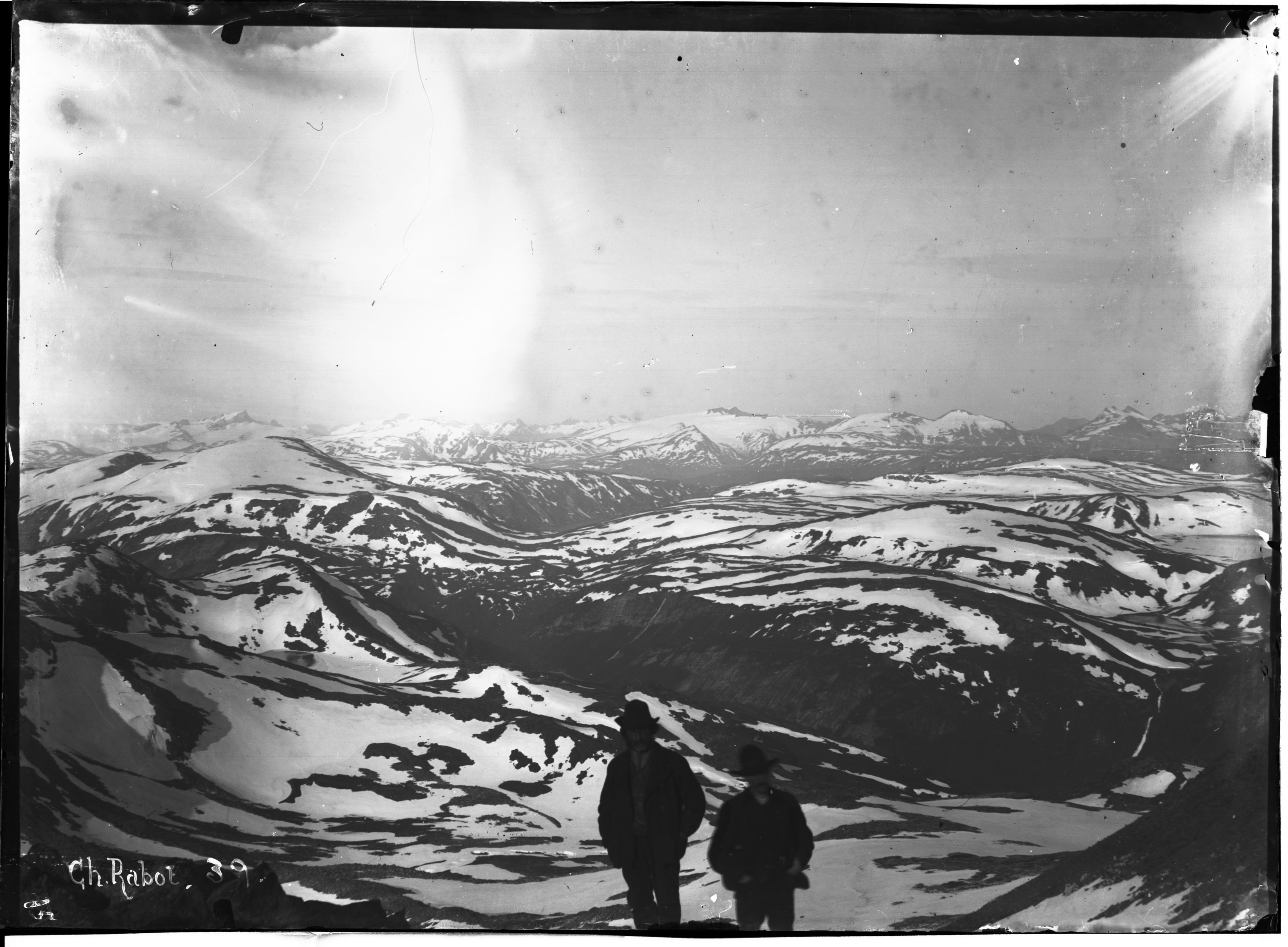 Black and white photograph of a snow-covered mountain range with two figures in the foreground.