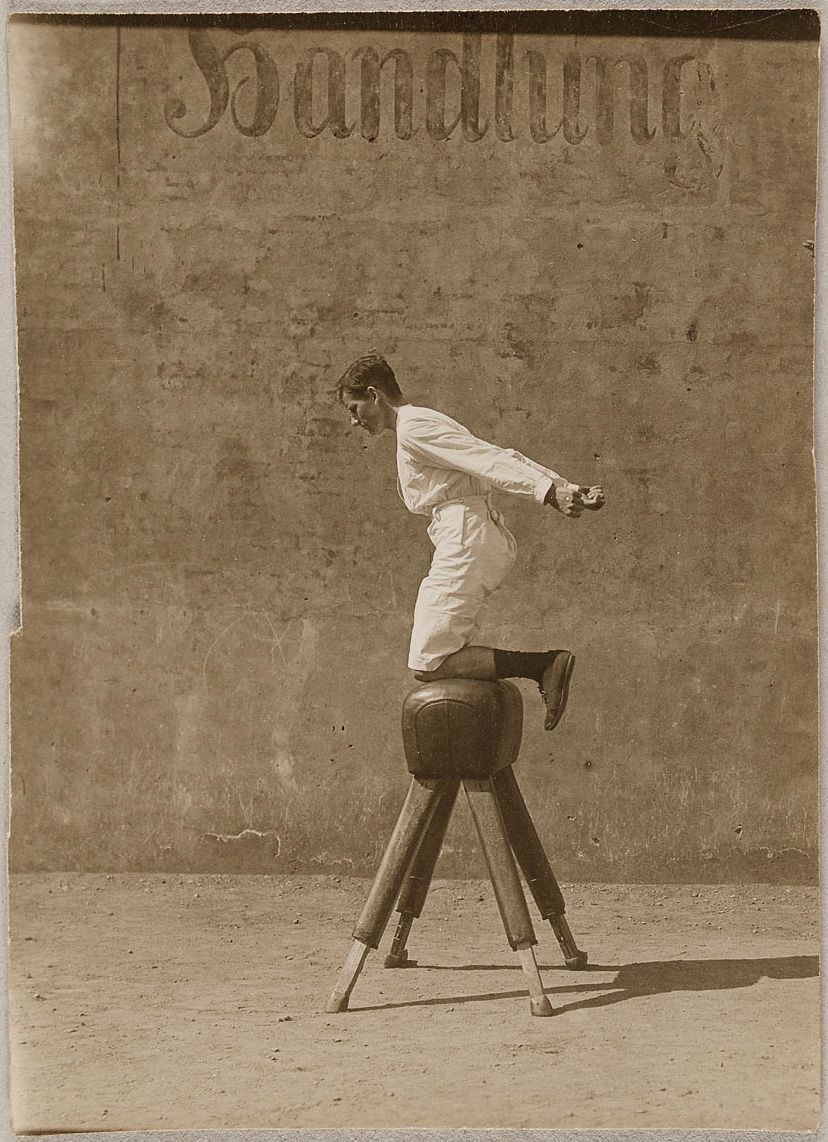 Sepia-toned photograph of a person riding a wooden horse in front of a weathered wall.