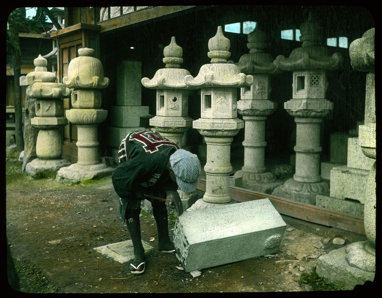 A person bends over a stone base in front of a row of ornate stone lanterns in a traditional Japanese setting.