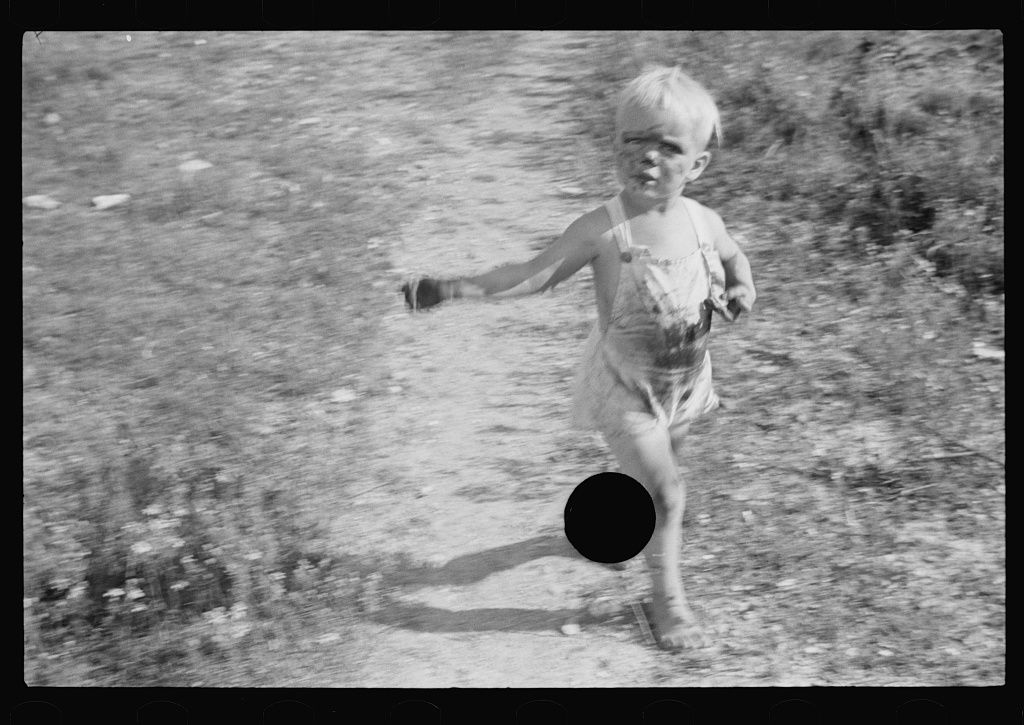 A black and white photograph of a young child running in a grassy field, with a black circle obscuring their lower body.