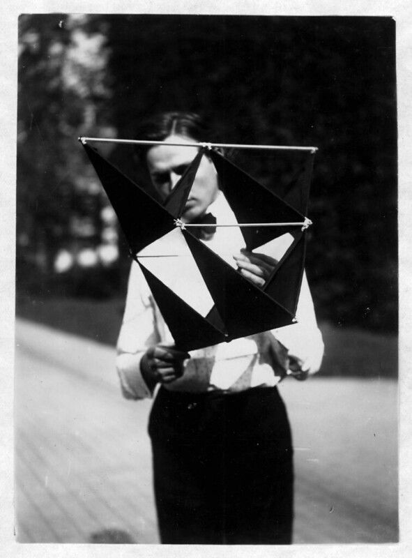 Black and white photograph of a person holding a geometric kite in front of their face.