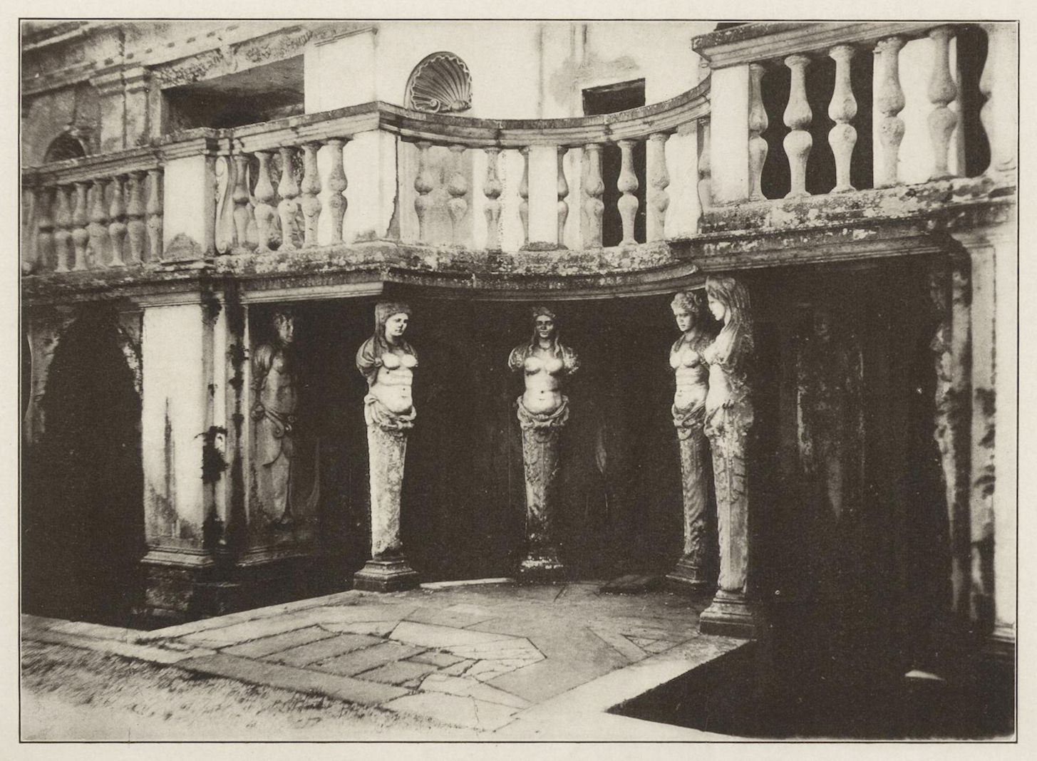 A black and white image of a classical architectural structure with columns, statues, and a paved floor.