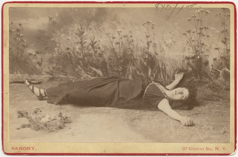 Sepia-toned photograph of a woman lying in a field of tall grass and wildflowers.