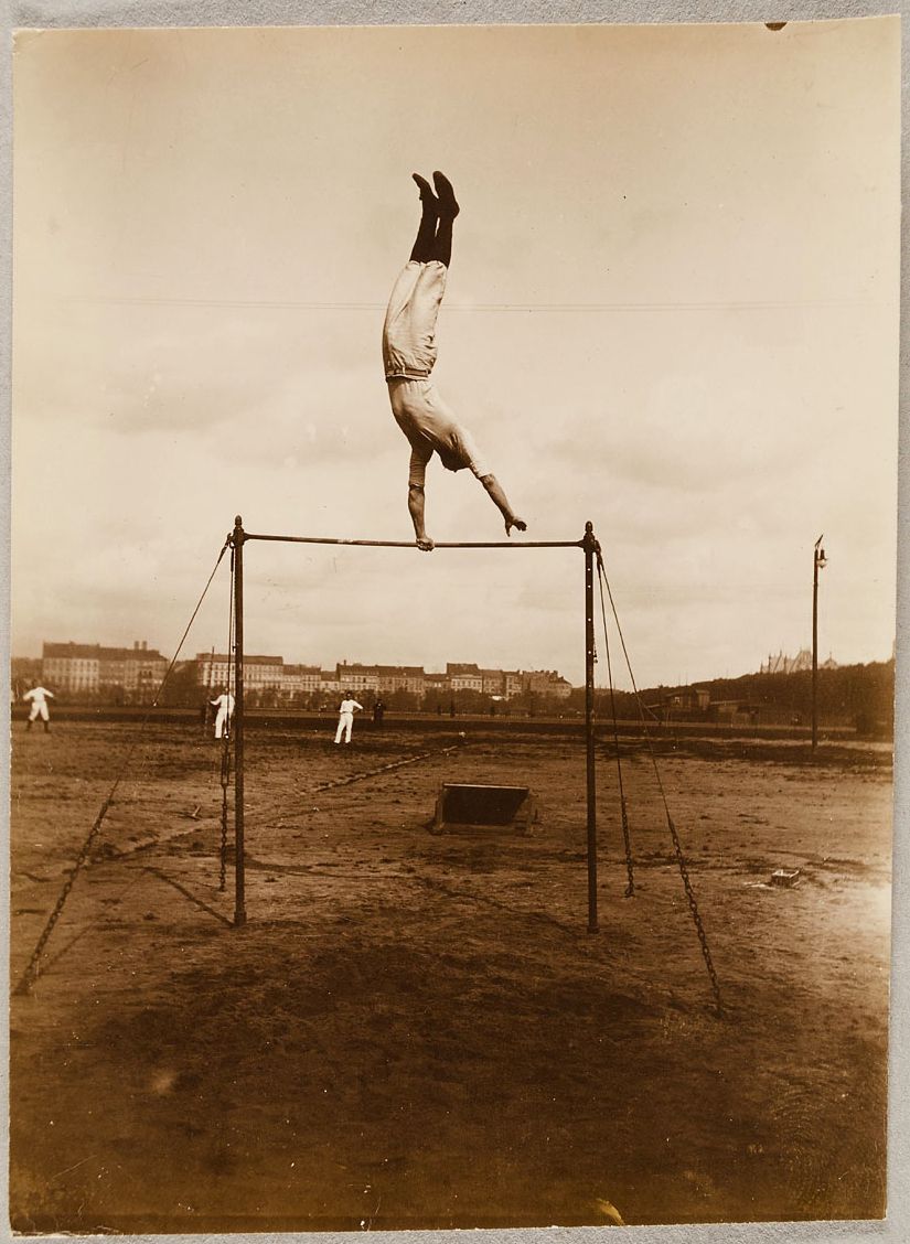 Vintage photograph of a man performing a gymnastic maneuver on a metal bar.