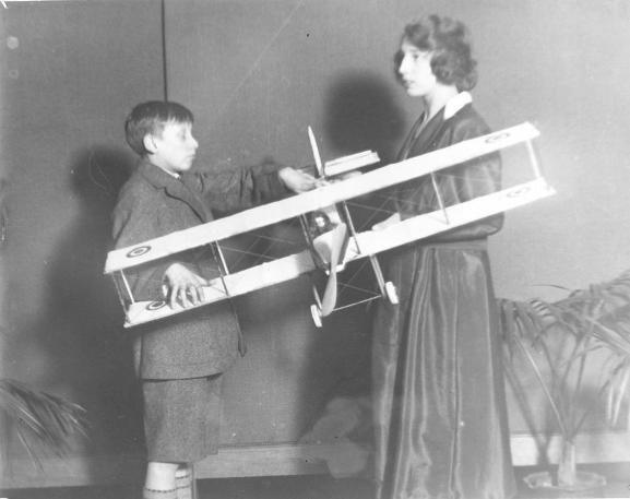 A black and white photograph of a young boy and a woman holding a model biplane.