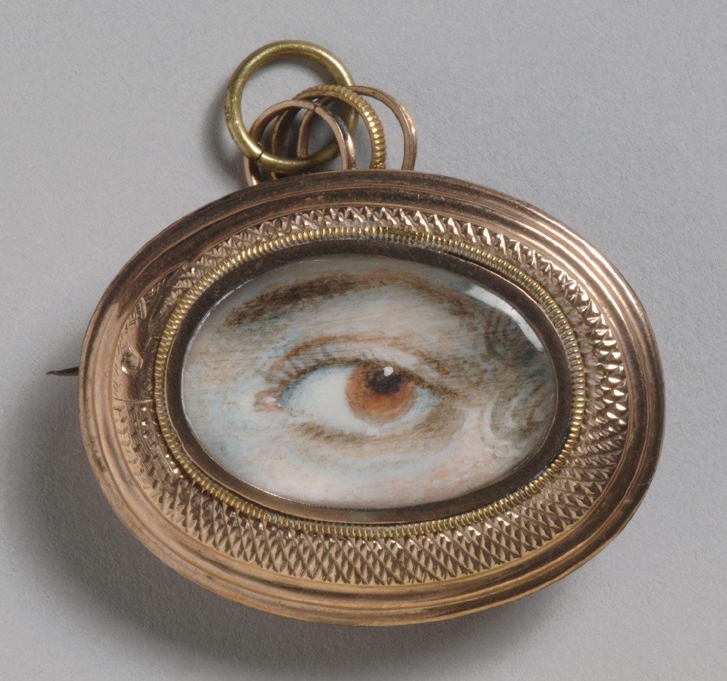 Close-up of an oval brooch with a painted eye in the center, set in a detailed gold frame.