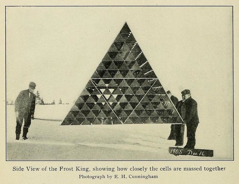 Vintage photograph of the Frost King, a large triangular structure made of cells, with two men standing beside it. The date 1905 Dec 16 is handwritten in the corner.