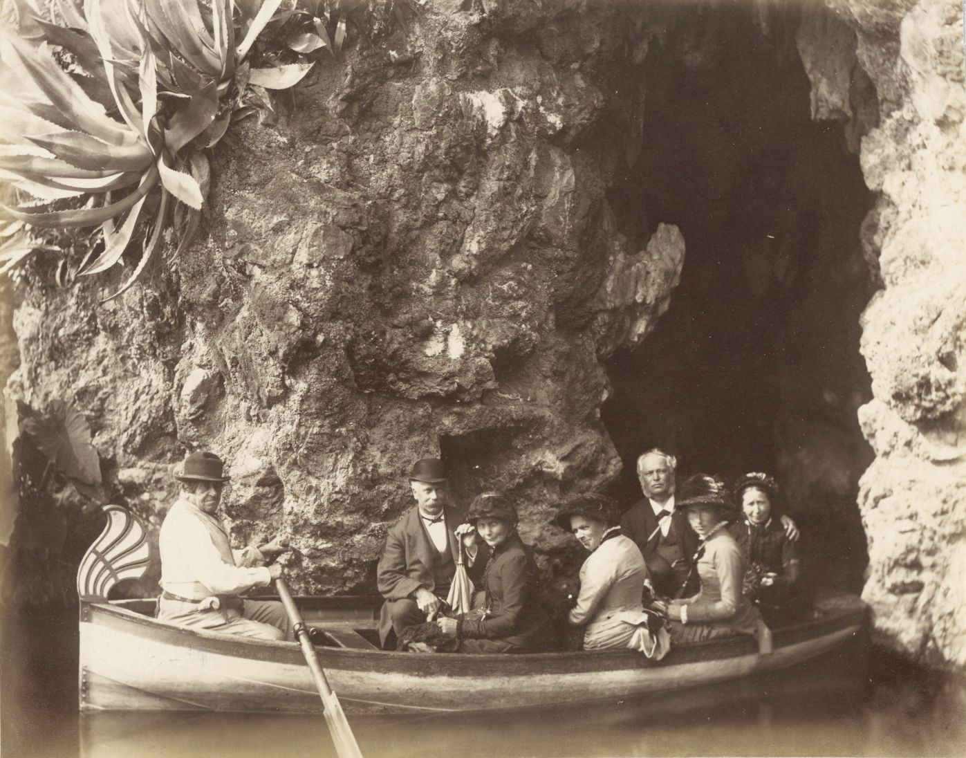 A vintage black and white photograph of a group of people in a boat inside a cave.