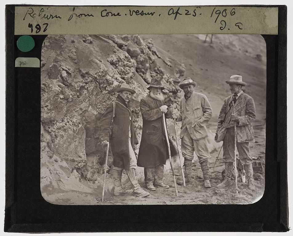 A black and white photograph of five men standing in a rugged, mountainous landscape. The photo appears to be a vintage glass slide, with handwritten text at the top reading 'Return from Cone. Vesuv. Af 25. 1906' and a number '987' in the upper left corner.