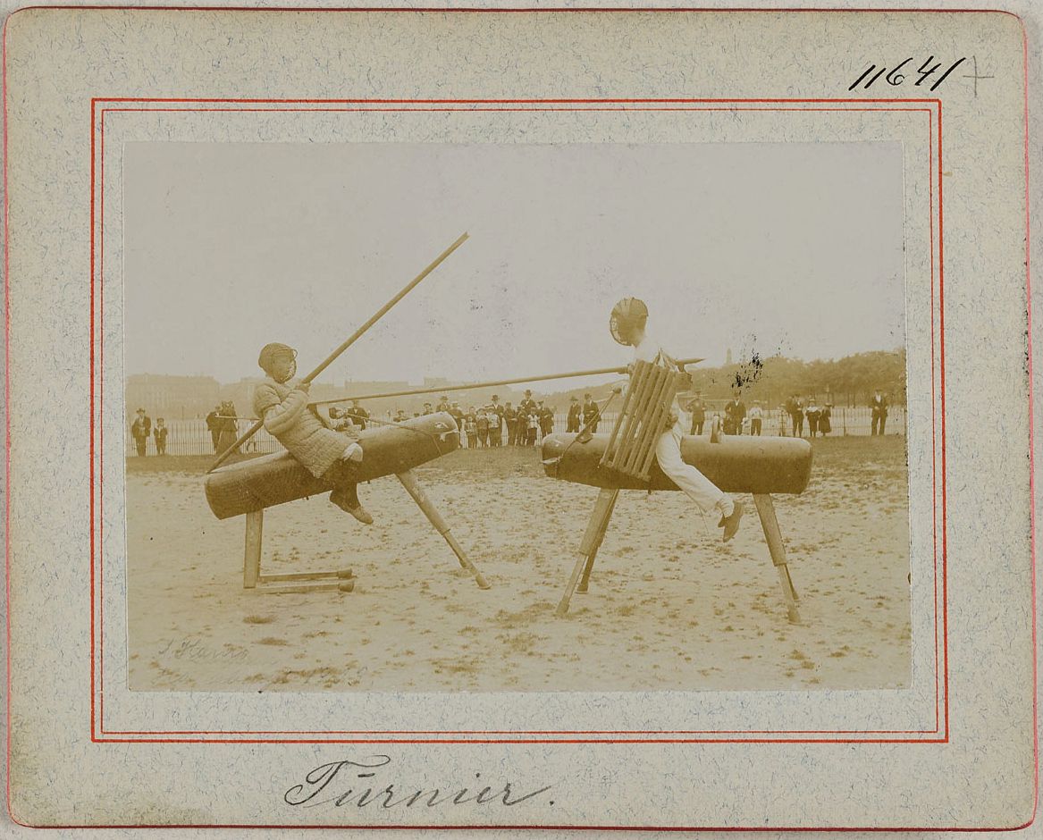 A vintage sepia-toned photograph of two boys on a peculiar balancing structure, with a crowd in the background.