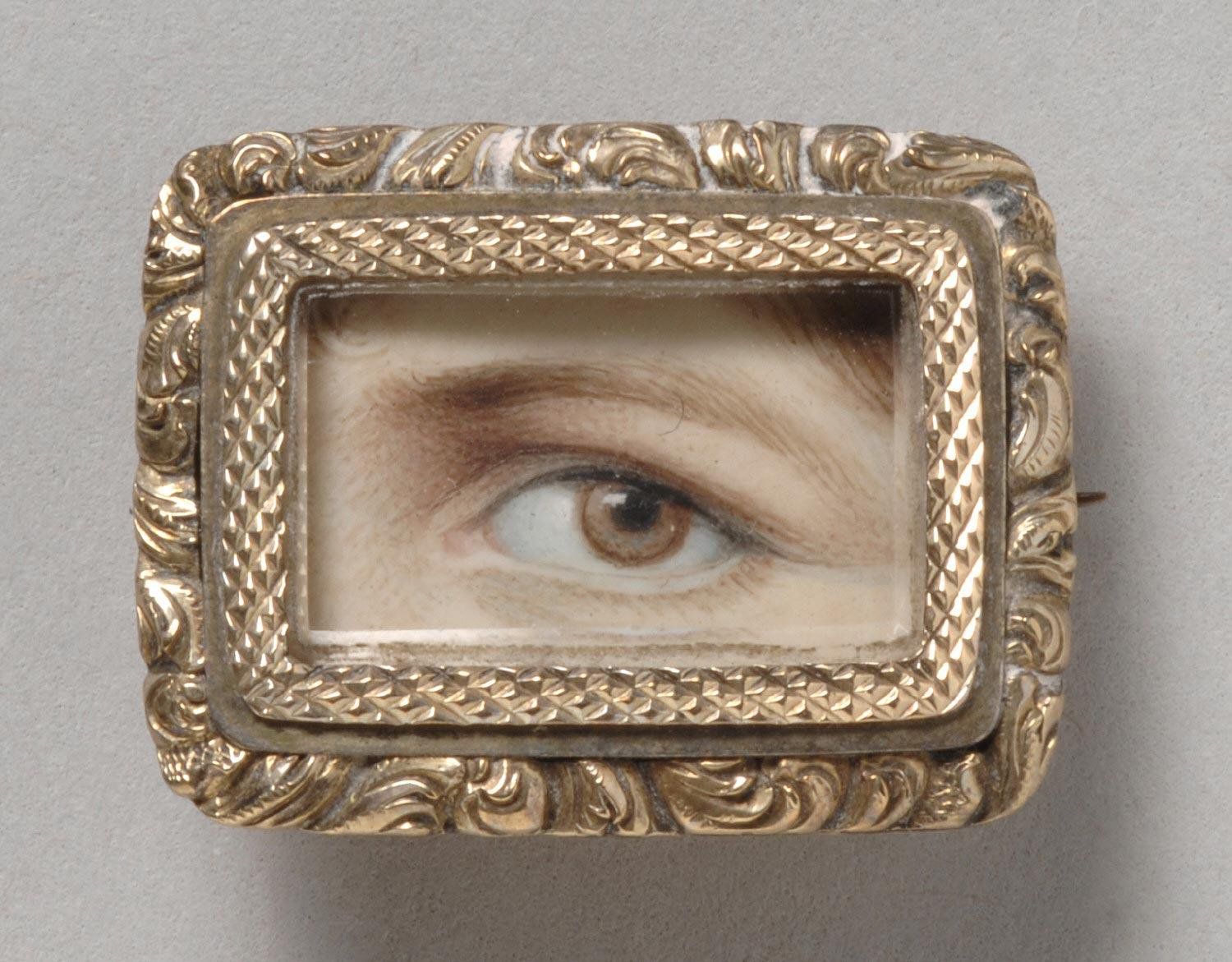 Close-up of a rectangular gold brooch featuring a miniature painting of a realistic human eye.