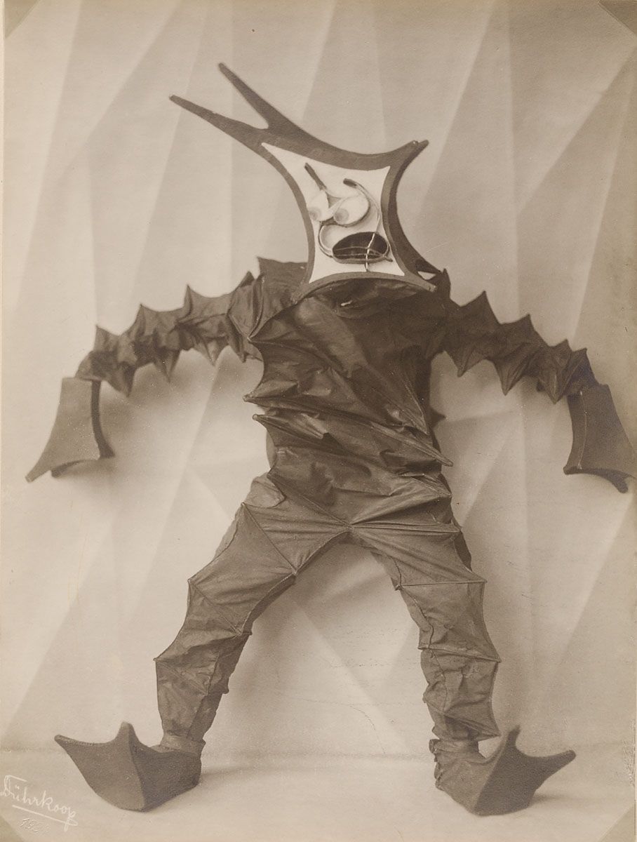 A vintage black and white photograph of a person in a cardboard costume with wings and a mask.