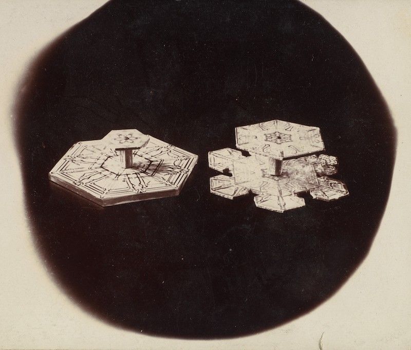 Vintage photograph of two snow crystals against a black background.