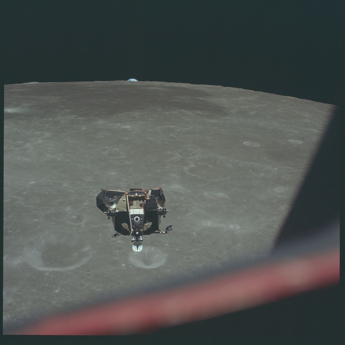 A photograph of the lunar module descending towards the moon's surface, with Earth visible in the distance.
