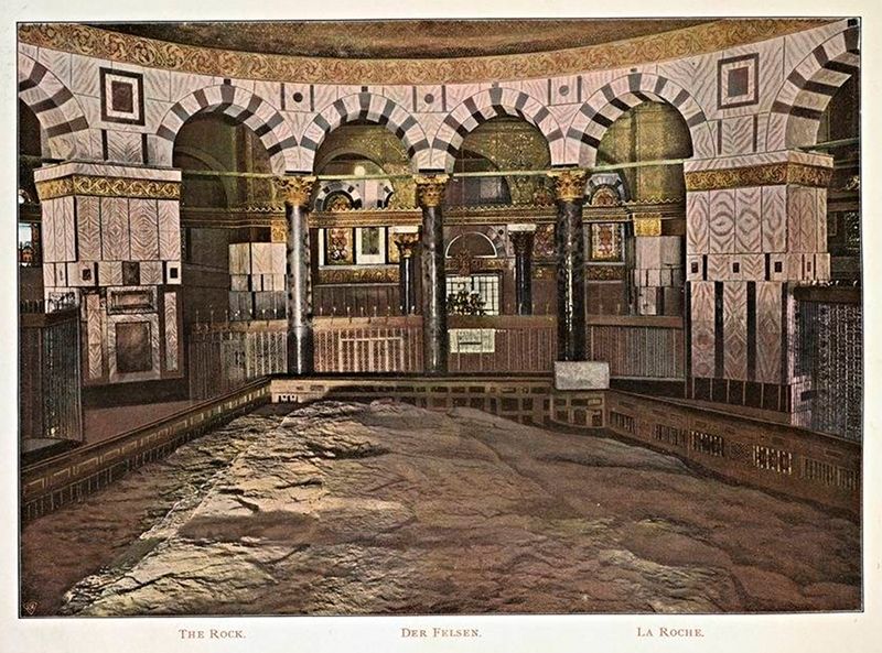 Interior view of a historical religious building with a large rock in the foreground, featuring arches, columns, and intricate mosaics.