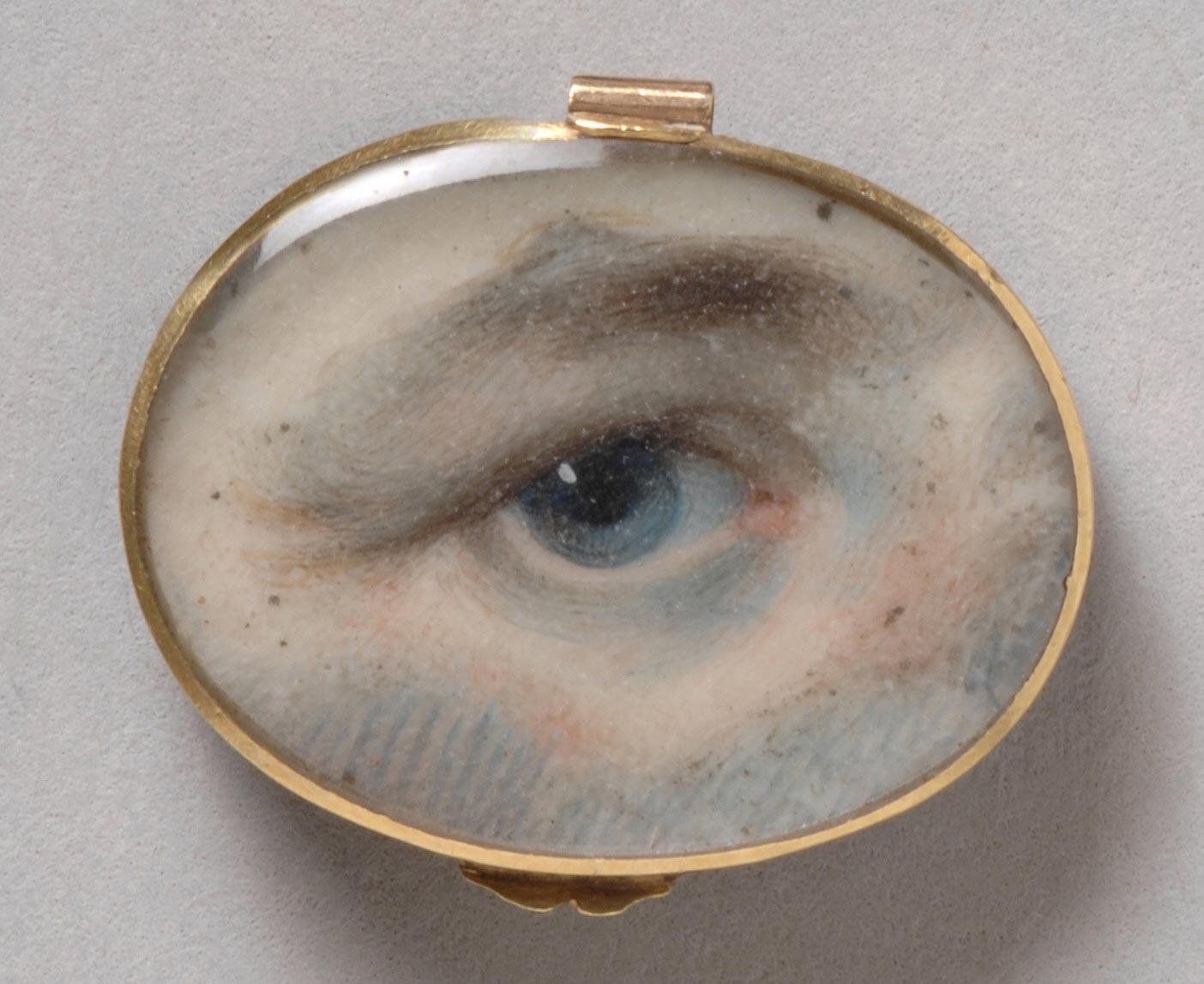 Close-up of a blue eye painted inside a gold locket.